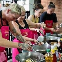 Vibrant cooking class in Thailand with participants wearing pink aprons, preparing dishes with various spices and ingredients.
