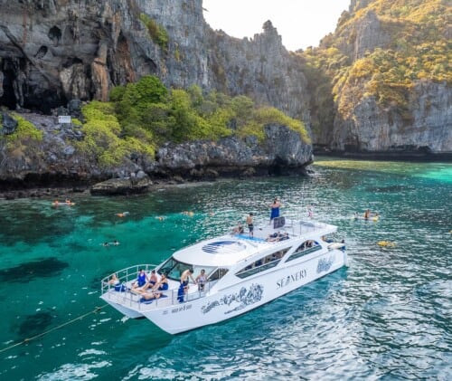 Crystal-clear turquoise boat cruise exploring limestone cliffs and lush green scenery in Thailand.