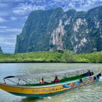Boat cruising in scenic river surrounded by lush mountains in Thailand.