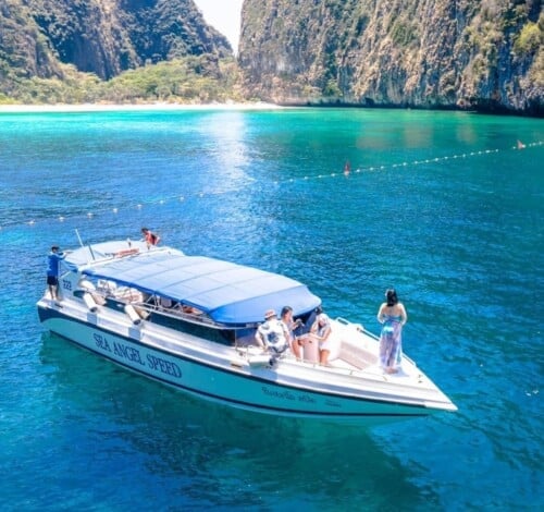 Secluded boat cruising in Thailand's turquoise waters with scenic cliffs in the background.